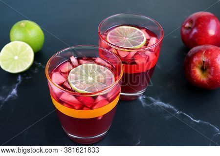 Two Glasses Of Red Wine Sangria On The Table With Blurry Limes And Apples In The Background