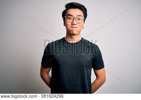 Young handsome chinese man wearing black t-shirt and glasses over white background puffing cheeks with funny face. Mouth inflated with air, crazy expression.
