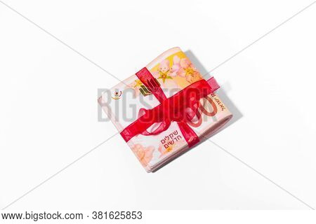 100 New Israeli Shekels Banknotes Folded In Half And Tied With A Red Ribbon On A Light Background.