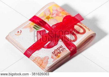 100 New Israeli Shekels Banknotes Folded In Half And Tied With A Red Ribbon Close-up On A Light Back