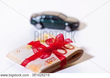 100 New Israeli Shekels Notes Are Folded In Half And Tied With A Red Ribbon In The Foreground. Car M