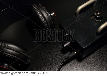 The Full Size Headphones Are Placed With A Tube Preamp On A Black Background.