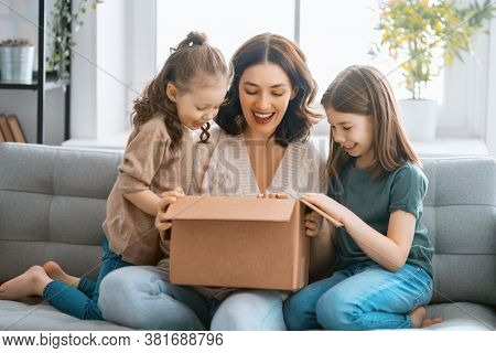 Mother and daughters are unpacking cardboard box at home.