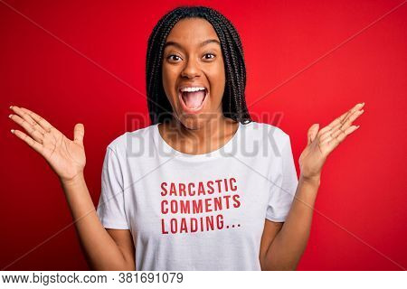 Young african american woman wearing sarcasm coments text on t-shirt over red background very happy and excited, winner expression celebrating victory screaming with big smile and raised hands