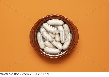 German White Sausage Boiled In A Brown Pot, Isolated On Orange Background. Top View Of Weisswurst, B