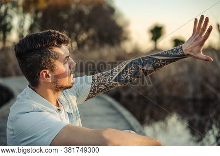 Young Tattooed Man Trying To Cover The Sun With His Hand On Outdoor Environmen