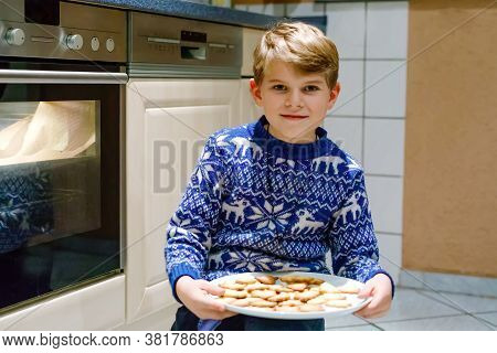 Cute Funny Blond Kid Boy Baking Muffins In Domestic Kitchen. Child Having Fun With Helping, Sitting 