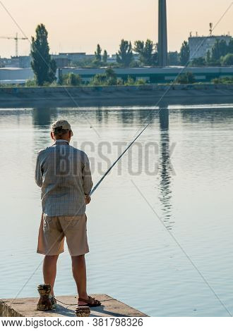 Fisherman At The Edge Of A Lake In Bucharest, Holding A Fishing Rod. Man Fishing.