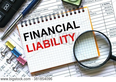 Text Financial Liability On Notepad With Calculator, Clips, Pen On Financial Report