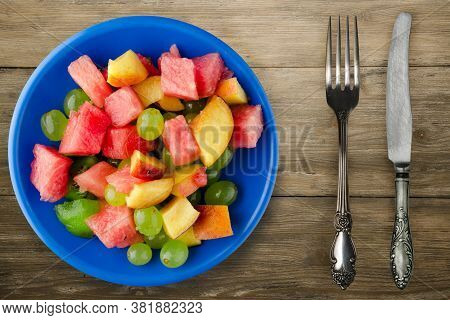 Fruit Salad On A Brown Wooden Background. Vegetarian Salad Of Fruit On A Blue Plate With Fork Ank Kn
