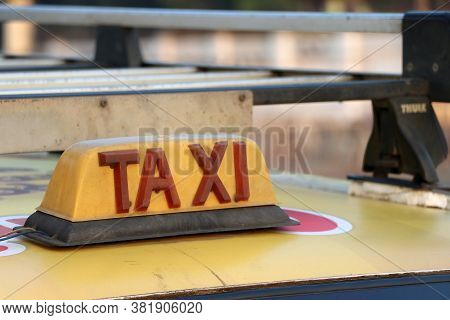 Taxi Light Sign Or Cab Sign In Drab Yellow Color With Red Text On The Car Roof At The Street Blurred
