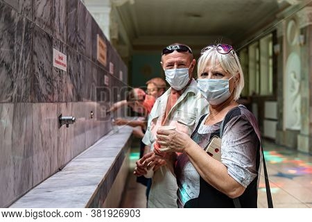 Tourists Of Retirement Age Drink Mineral Water In The Open Narzannaya Gallery In Protective Masks