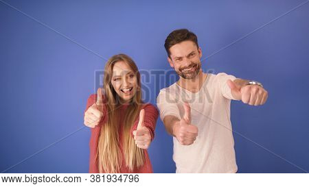 Young Happy Couple With Thumbs Up Isolated On The Blue Background. Copy Space.