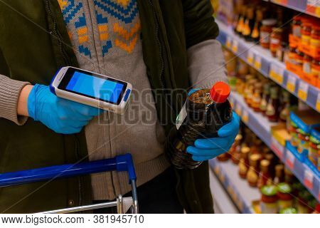 A Customer Wearing Medical Protective Gloves Holds A Barcode Scanner And Scans The Product. Cropped 