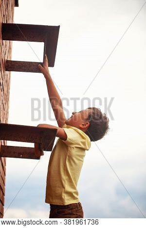 Teenage Boy Climbs A Brick Wall To The Roof. Child In Danger. Climbs On A Construction Site In An Un