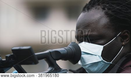 Close Up, African Black Videographer With Medikal Mask Looking Through The Viewfinder On Video Camer