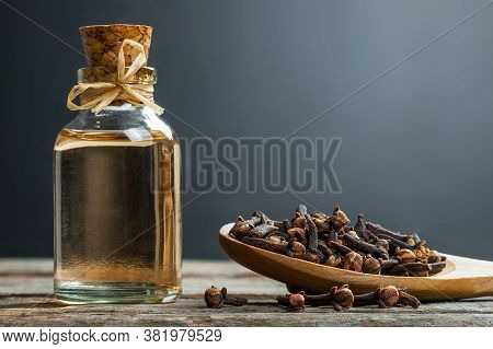 Close Up Glass Bottle Of Clove Oil And Cloves In Wooden Spoon On Wooden Table. Essential Oil Of Clov