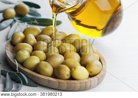 Glass Bottle Of Olive Oil And Olive Tree Branch, Raw Turkish Green Olive Seeds And Leaves On  Rustic