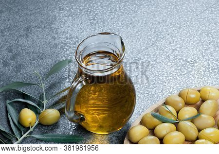 Glass Bottle Of Olive Oil And Olive Tree Branch, Raw Turkish Green Olive Seeds And Leaves On Rustic 
