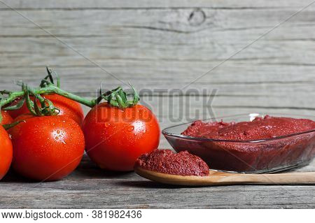 Tomato Paste In Wooden Spoon And Ripe Fresh Grape Tomatoes On Wooden Background. Cherry Tomatoes. To