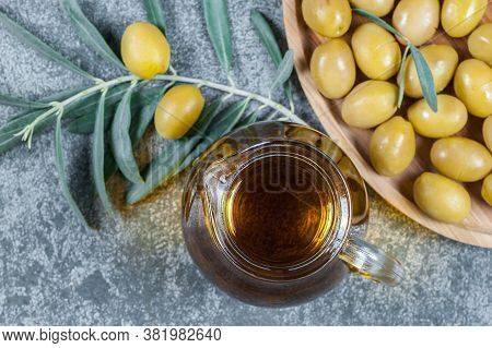 Glass Bottle Of Olive Oil And Olive Tree Branch, Raw Turkish Green Olive Seeds And Leaves On Rustic 
