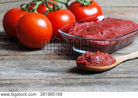 Tomato Paste In Wooden Spoon And Ripe Fresh Grape Tomatoes On Wooden Background. Cherry Tomatoes. To