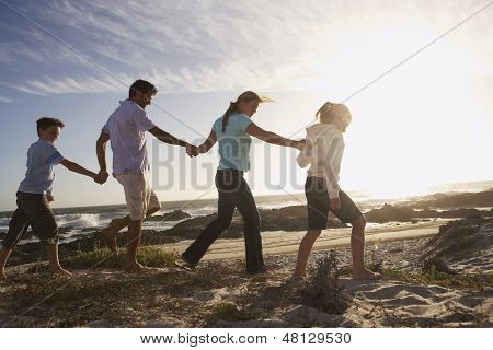 Vista laterale di genitori e bambini camminare mano nella mano sulla spiaggia