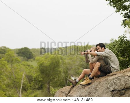 Vista lateral de comprimento total de um homem jovem, apontando para o vista por mulher em pedra com binóculos