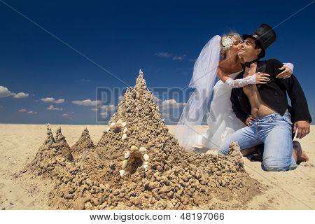 En ung och vacker nyligen gift par njuter på stranden nära sand slott vid havet kanten