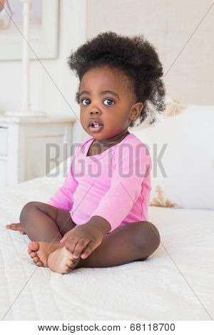 Baby girl in pink babygro sitting on bed at home in the bedroom
