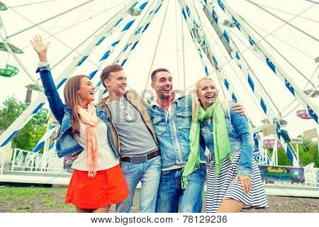 leisture, amusement park and friendship concept - group of smiling friends waving hands with ferris wheel on the back