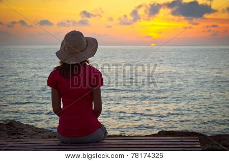 Young woman in hat sitting and looking at sunset