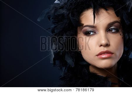 Mystical look of beauty covered in black feather boa, wearing makeup with strasses.
