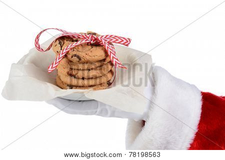 Santa Claus holding a plate with a stack of chocolate chip cookies tied with a ribbon. Only Santa's gloved hand and red sleeve are shown as he holds the plate over a white background.