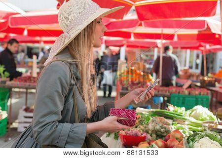 Attractive blonde woman with straw hat paying vegetables on marketplace.
