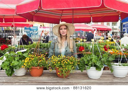 Attractive blonde woman with straw hat posing on flower marketplace.