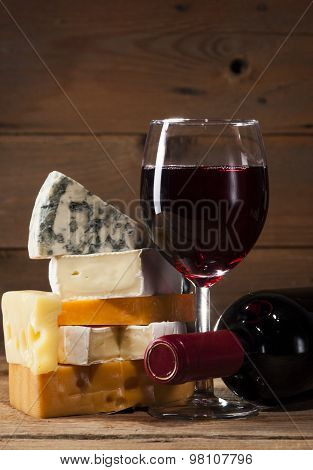 Red wine with various types of cheese on wooden background
