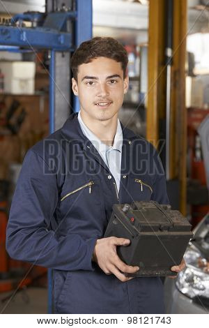 Apprentice Mechanic Holding Car Battery In Auto Repair Shop