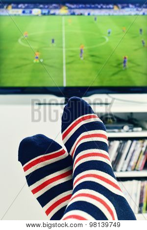 closeup of the feet of a man who is watching a soccer match in the TV, wearing striped socks