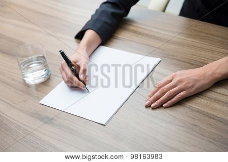 Closeup Of A Business Woman's Hands While Writing Down Some Essential Information. A Glass Of Water,