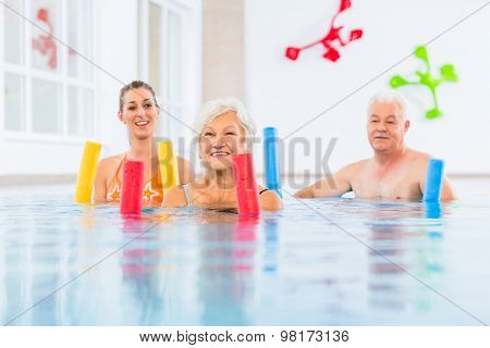 Group  or young and senior people in aquarobic fitness swimming pool exercising with  pool noodle