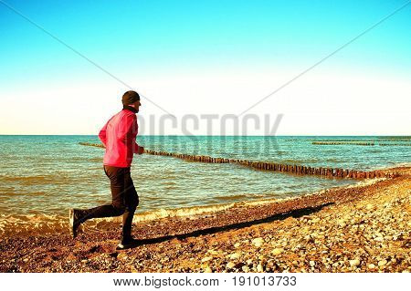 Tall Man In Dark Sportswer Running And Exercising On Stony Beach At Breakwater.