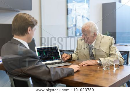Young financial advisor sitting in front of laptop, consulting senior client with his investment strategy.