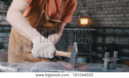 The blacksmith with a beard gives shape with the help of a hammer on the anvil to a red-hot metal productproduct