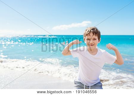 Confident Little Boy Showing His Muscles While Playing At The Beach