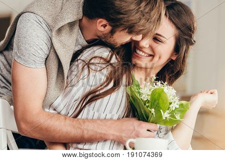 young casual couple embracing with bouquet of flowers at home