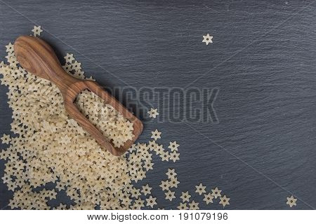 Star shaped noodles and olive wood scoop on black background of slate or stone. Top view