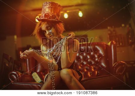 Redhaired girl sitting on sofa with chains in her hands and hat and glasses.  Studio photo