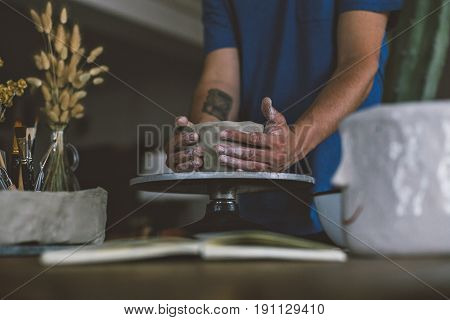 Close up of male hands working with clay on artisan working stand from dry wood surrounded by artistic workshop tools and implements creates poterry diy