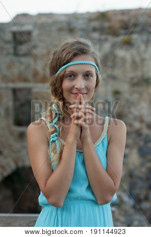 Young Blonde Woman Wearing Turquoise Top Standing Against Medieval Stone Wall And Smiling